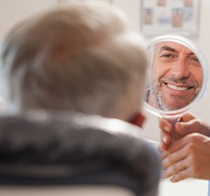 Man smiling while looking at reflection in handheld mirror