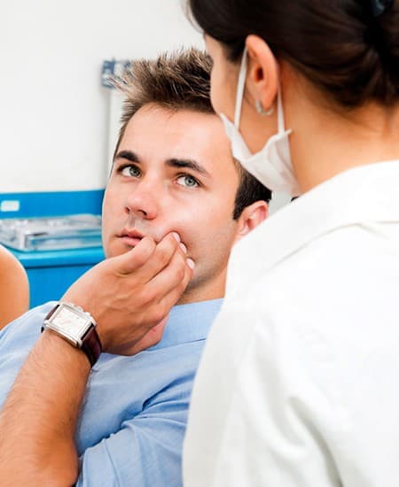 Man in dental chair holding cheek