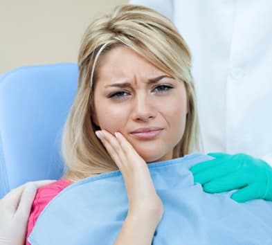 Woman in dental chair holding cheek