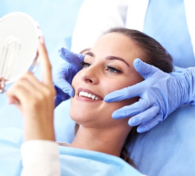 young woman sitting in dental chair and admiring her smile in hand mirror