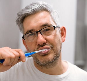 Older man with dental implants in Alexandria brushing his teeth.