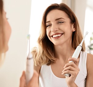 Woman with dental implants in Alexandria holding an electric toothbrush. 