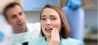 Woman in dental chair holding cheek