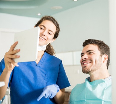 Dental assistant and patient smiling at treatment plan on tablet