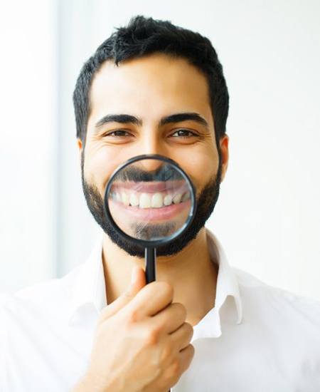 man using magnifying glass to show off results of at-home teeth whitening in Alexandria 