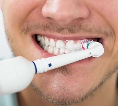 close up of man with short facial hair using electric toothbrush 