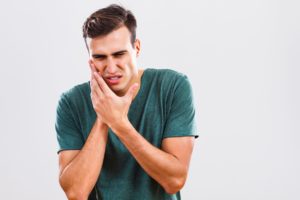 young man holding his face because of painful dental emergency 