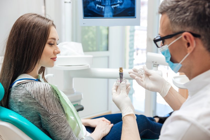 a young woman listens to her dentist who shows her how a dental implant works