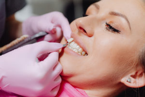 Gloved hands holding veneer by woman’s tooth